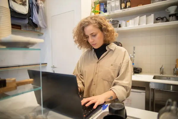 Frustrated small business owner leaning on a counter while struggling with website technical issues on a laptop.